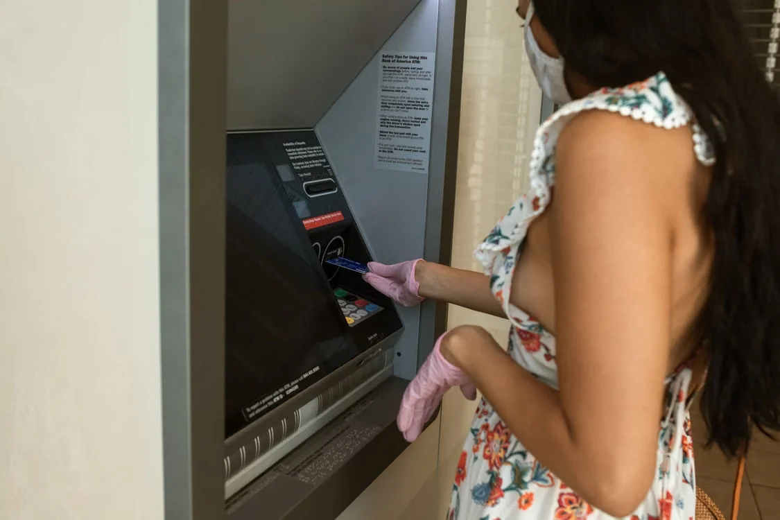 Egy maszkot viselő nő bankautomatánál kártyát használ, közeli nézetben.
